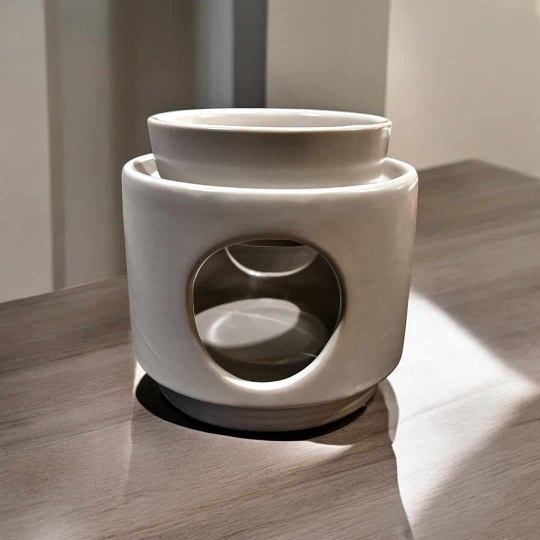 A white ceramic wax melt warmer with a two-piece design, featuring a detachable dish and a base, placed on a wooden surface.