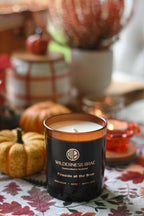 Fireside at the Brae unlit candle with  Wilderness Brae, Handcrafted in Scotland black and gold label. Amber jar sits on a table with autumn decor, including small pumpkins.
