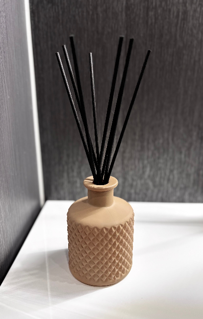 Reed diffuser with black reeds in a textured vase on a white surface.