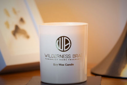 White candle with 'Wilderness Brand' logo on a wooden surface

