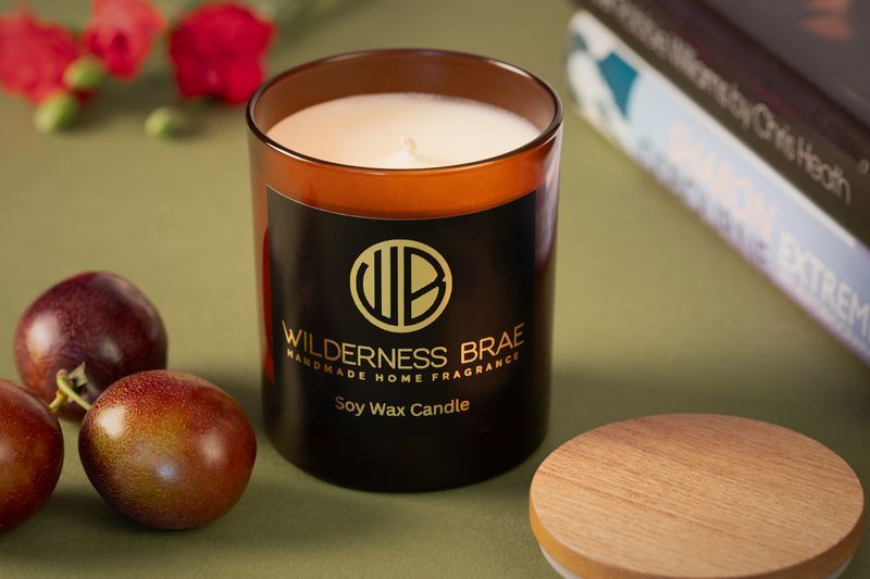 Rosebrae Velvet soy wax candle by Wilderness Brae Home Fragrance brand. On green table with books and plums in background. 