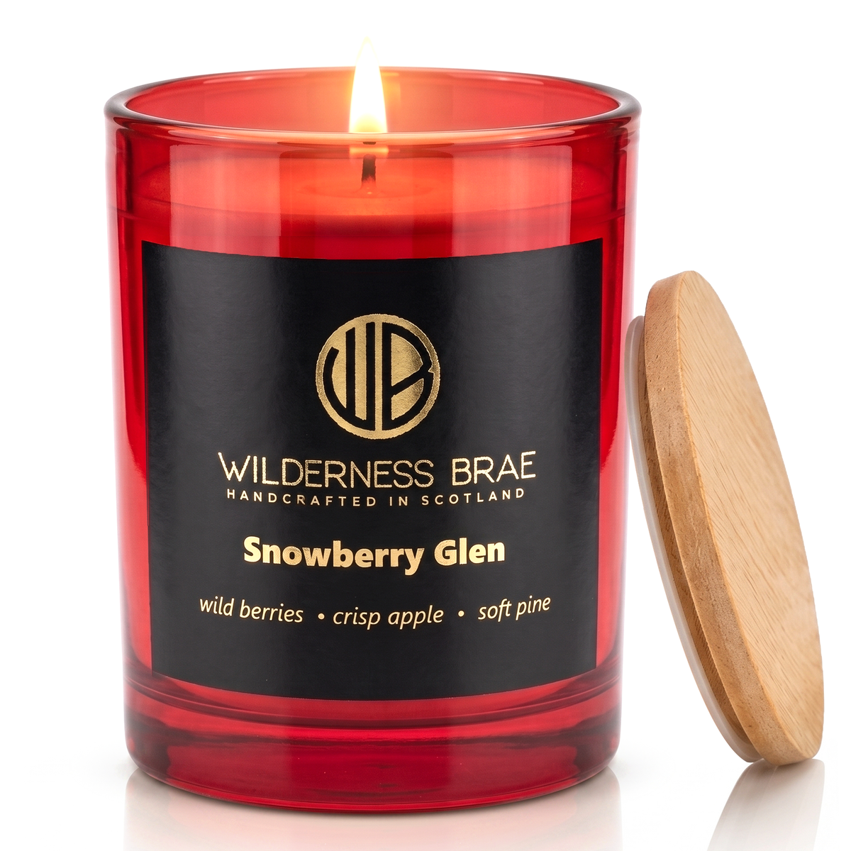 Snowberry Glen soy candle, handcrafted in Scotland by Wilderness brae.  Red glass jar candle with a black and gold label lit with a wooden lid leaning against it on a white background.