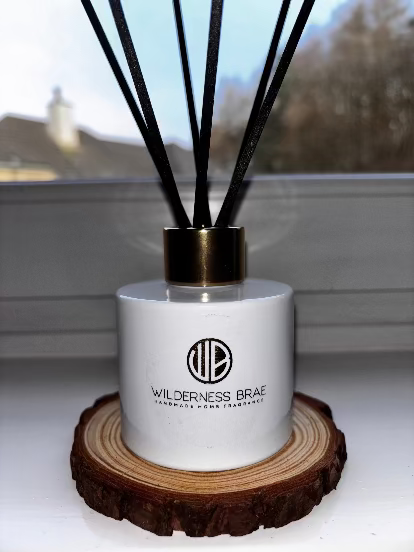 White and gold bottle reed diffuser with black fibre reeds on wooden coaster