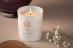 White candle with 'Wilderness Brae' branding on a beige surface with white flowers.