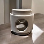 A white ceramic wax melt warmer with a two-piece design, featuring a detachable dish and a base, placed on a wooden surface.