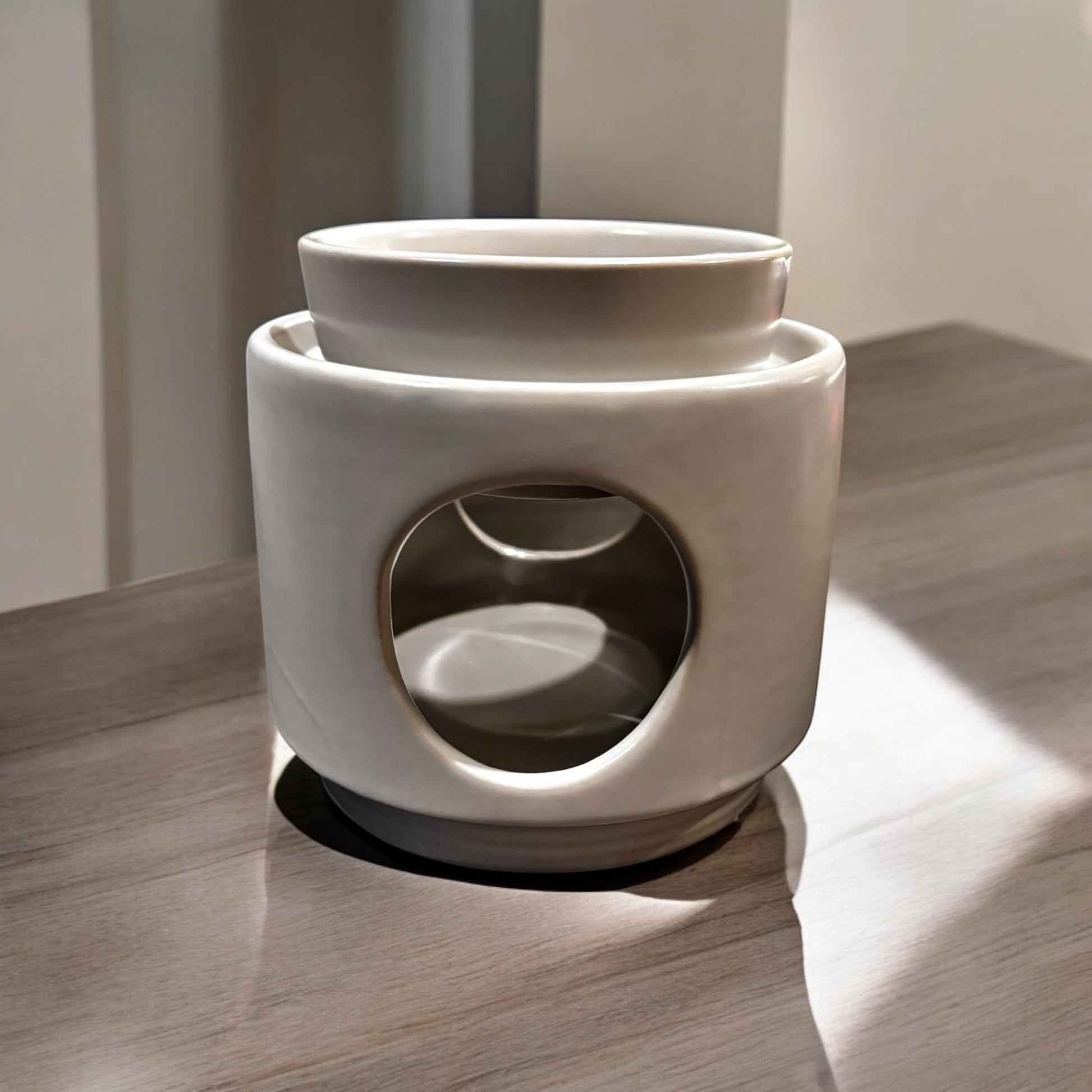 A white ceramic wax melt warmer with a two-piece design, featuring a detachable dish and a base, placed on a wooden surface.