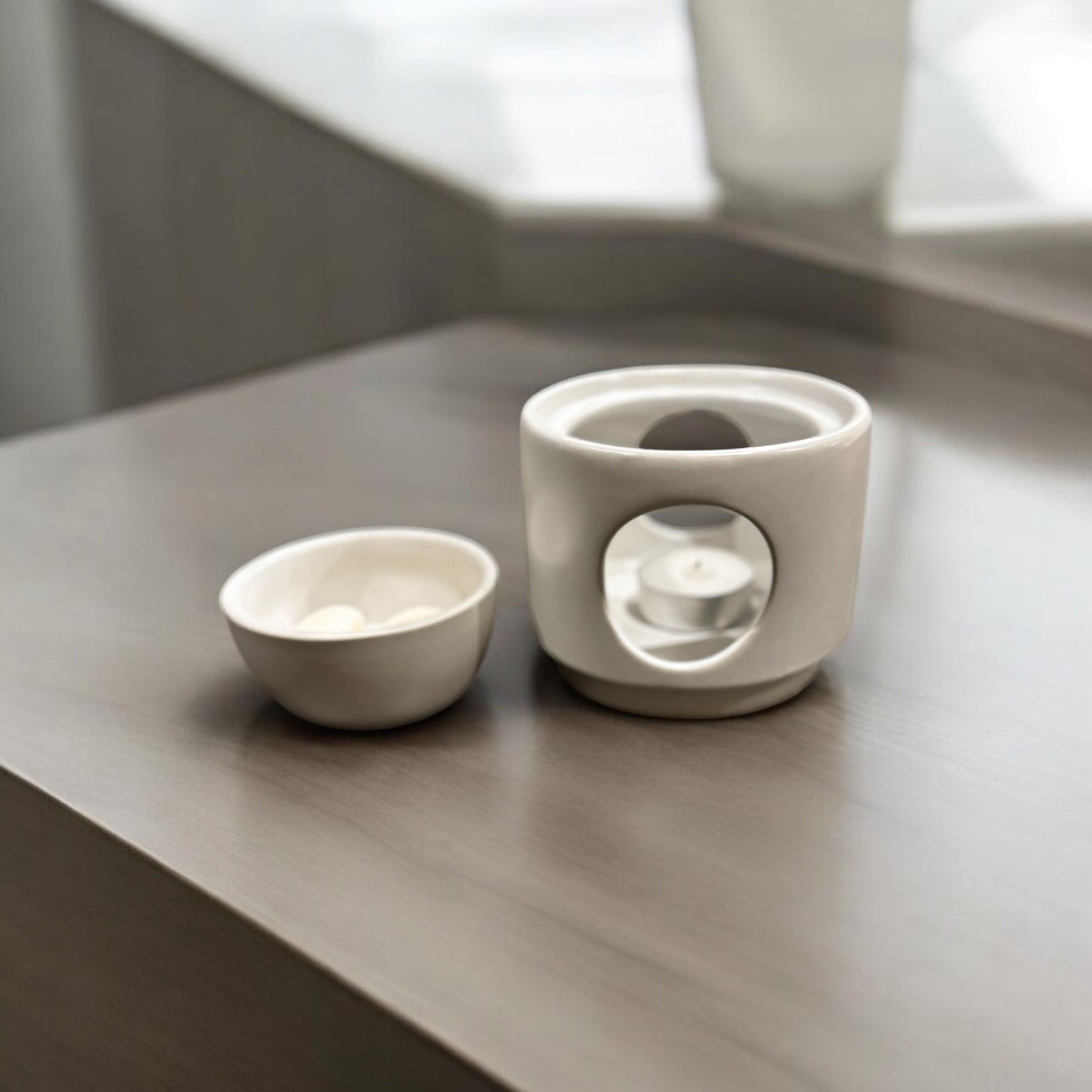 two-piece wax warmer in white on beige worktop- lid off with tealight in base and wax melts in lid bowl