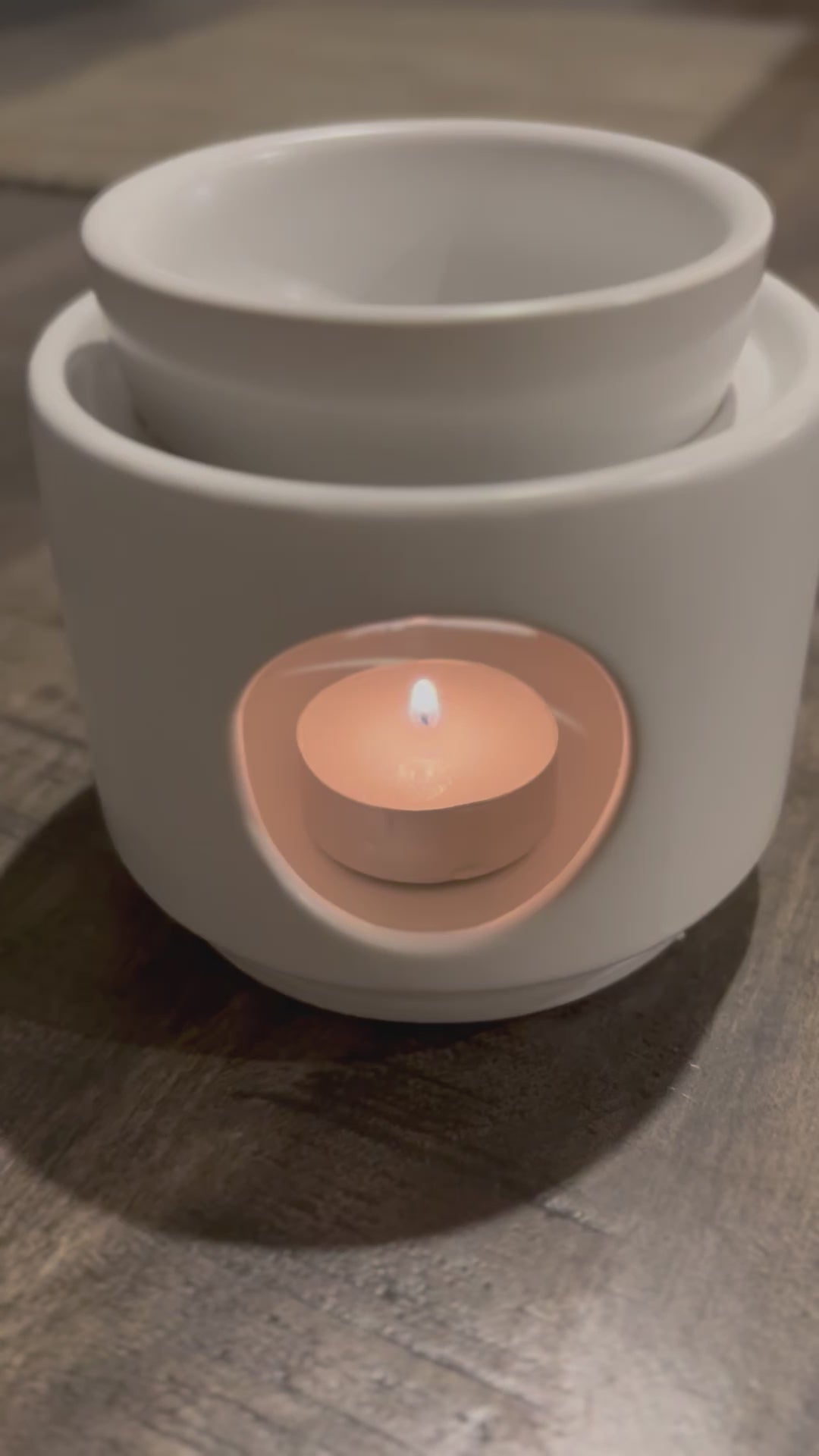 white wax warmer with lit tealight in situ. Person putting wax melts in the top lid bowl